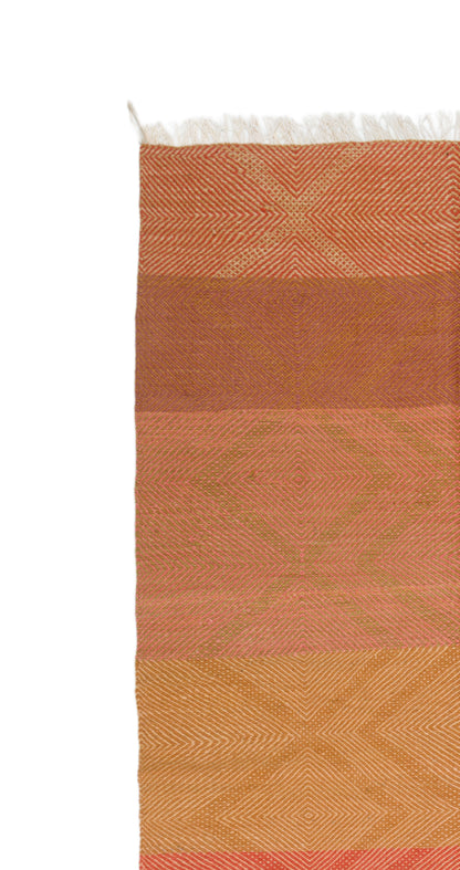 A close-up of a Zanafi rug with horizontal bands in terracotta, rust, peach, and golden yellow, featuring a subtle geometric pattern and white fringe at the top, shown against a plain white background.