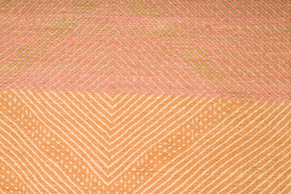 A close-up of a woven Zanafi rug with a geometric chevron pattern, split horizontally into two sections: a top section in dusty pink and a bottom section in warm peach-orange, both with fine striped texture.