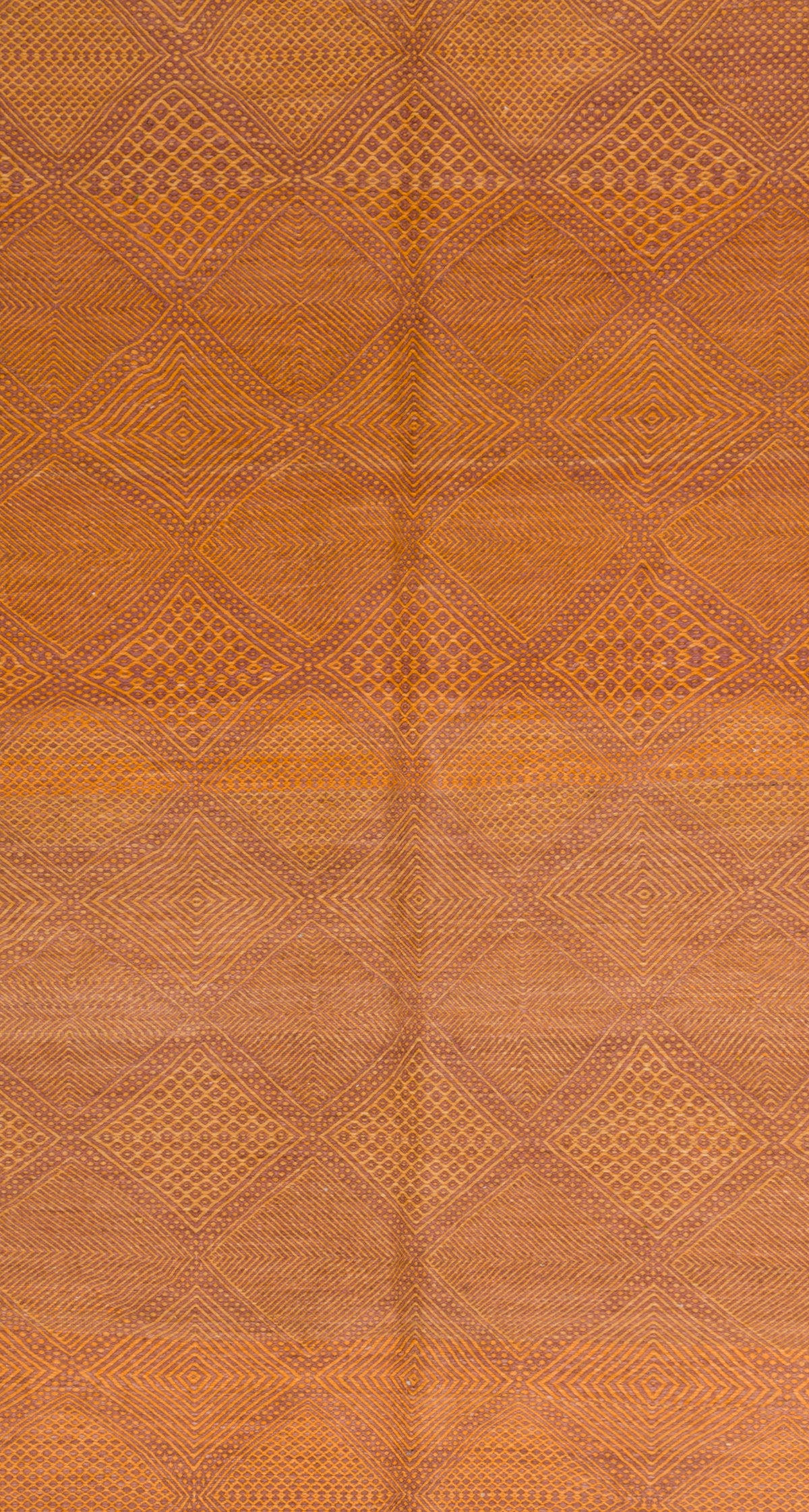 A close-up of a wool Moroccan rug in warm orange-brown tones, showing a repeating diamond pattern and subtle central seam.