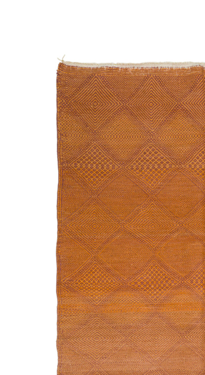 A close-up of a woven textile or rug in warm rust orange with a subtle diamond pattern, shown against a plain white background.