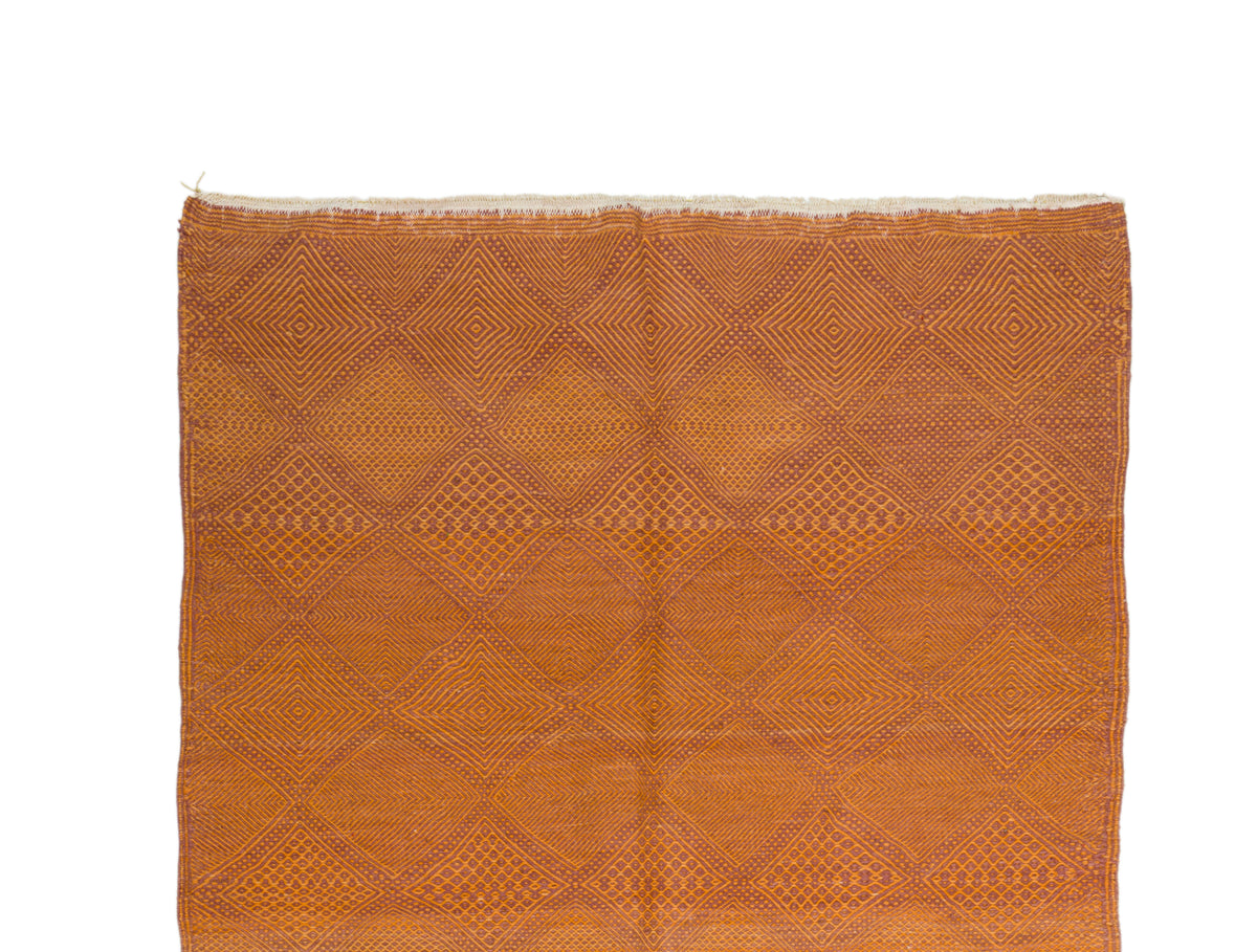 A square woven Zanafi rug in a warm rust-orange color, featuring a geometric diamond pattern and frayed edges, shown flat against a white background.