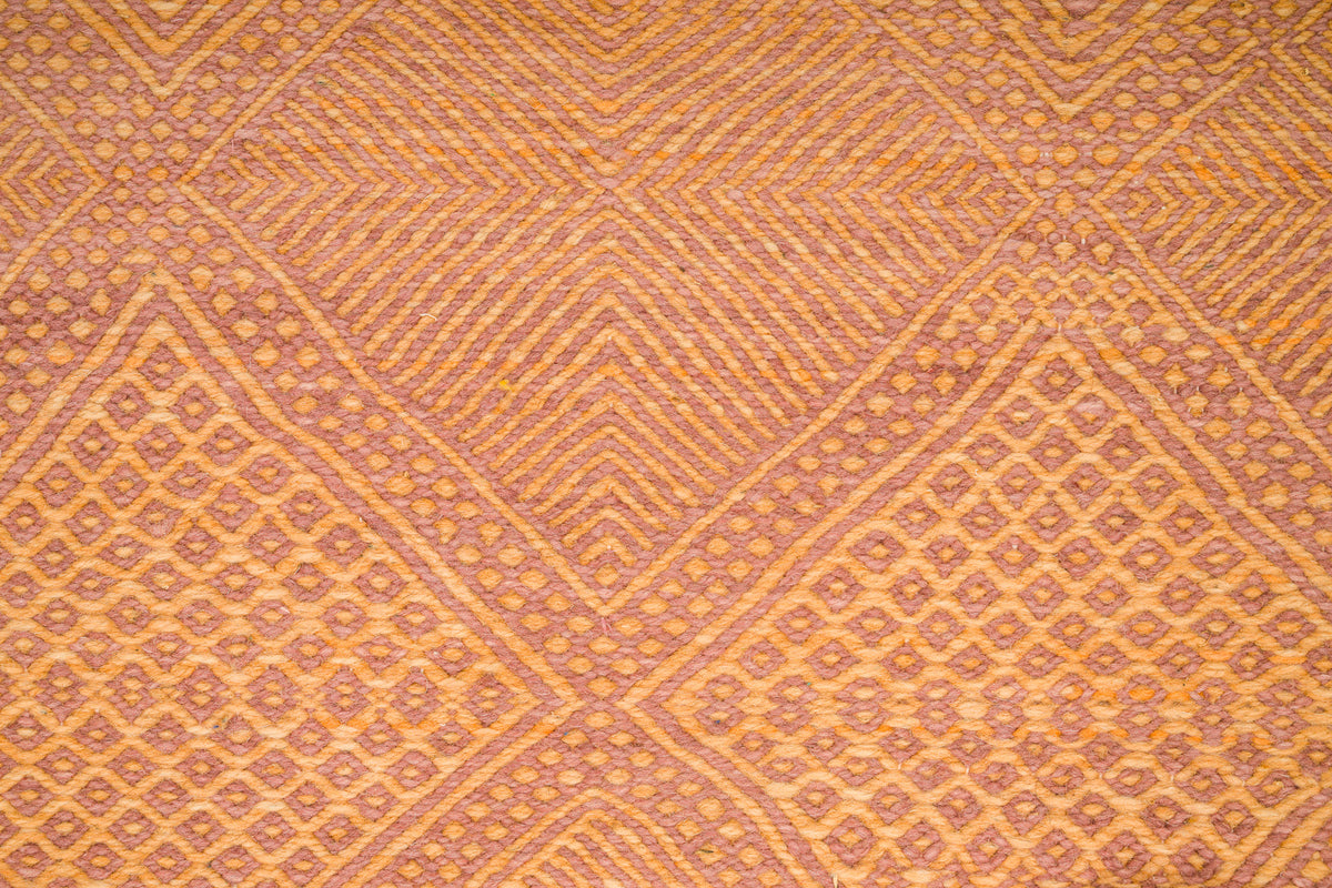 A close-up of a woven Zanafi rug with a geometric diamond pattern in warm orange, tan, and brown tones.