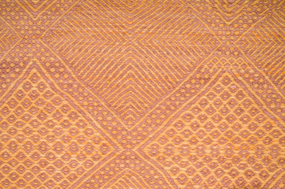 A close-up of a woven Zanafi rug with a geometric diamond pattern in warm orange, tan, and brown tones.