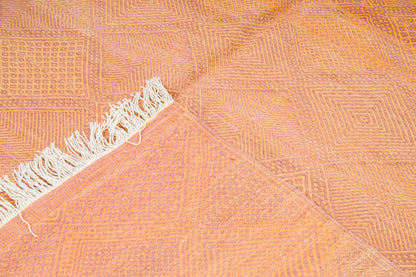 A close-up of a peach-orange woven rug with a geometric pattern and white fringe along one edge.