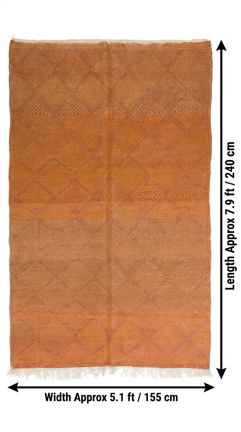 An orange-brown woven rug with a diamond pattern and white fringe, shown with dimension arrows.