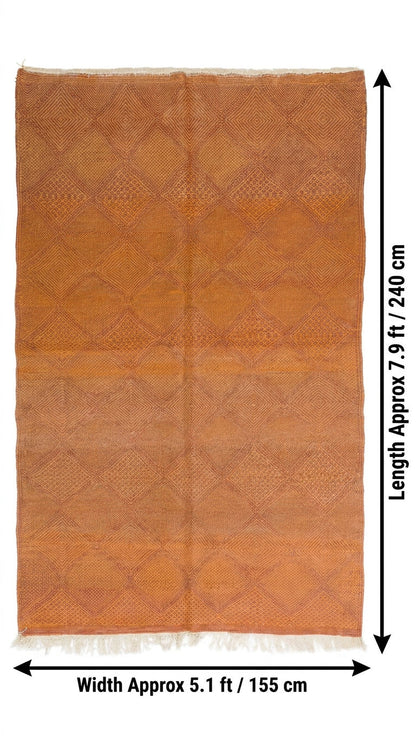 An orange-brown woven rug with a diamond pattern and white fringe, shown with dimension arrows.