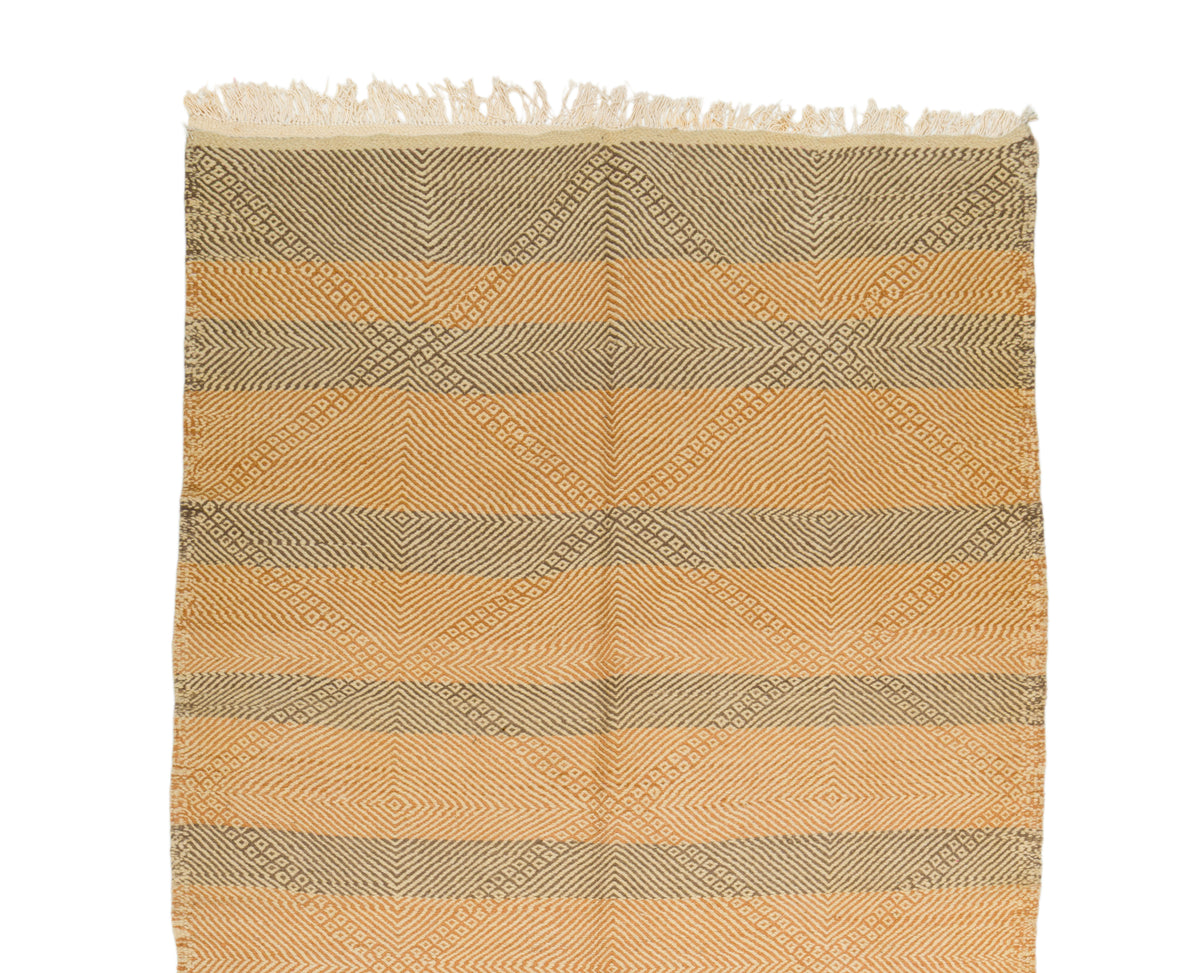 A rectangular wovenrug with fringe on one end, featuring horizontal stripes and a diamond lattice pattern in warm tan, beige, and taupe tones on a white background.