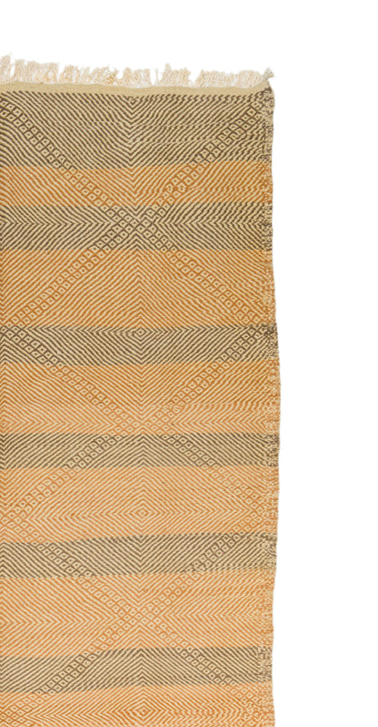 A close-up of a woven ru with horizontal stripes in warm beige and muted taupe, featuring a subtle geometric diamond pattern and fringed edges at the top, shown against a white background.