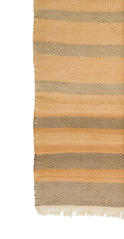 A close-up of a woven rug with horizontal stripes in warm beige, tan, and taupe, featuring a textured geometric pattern and fringed edges.