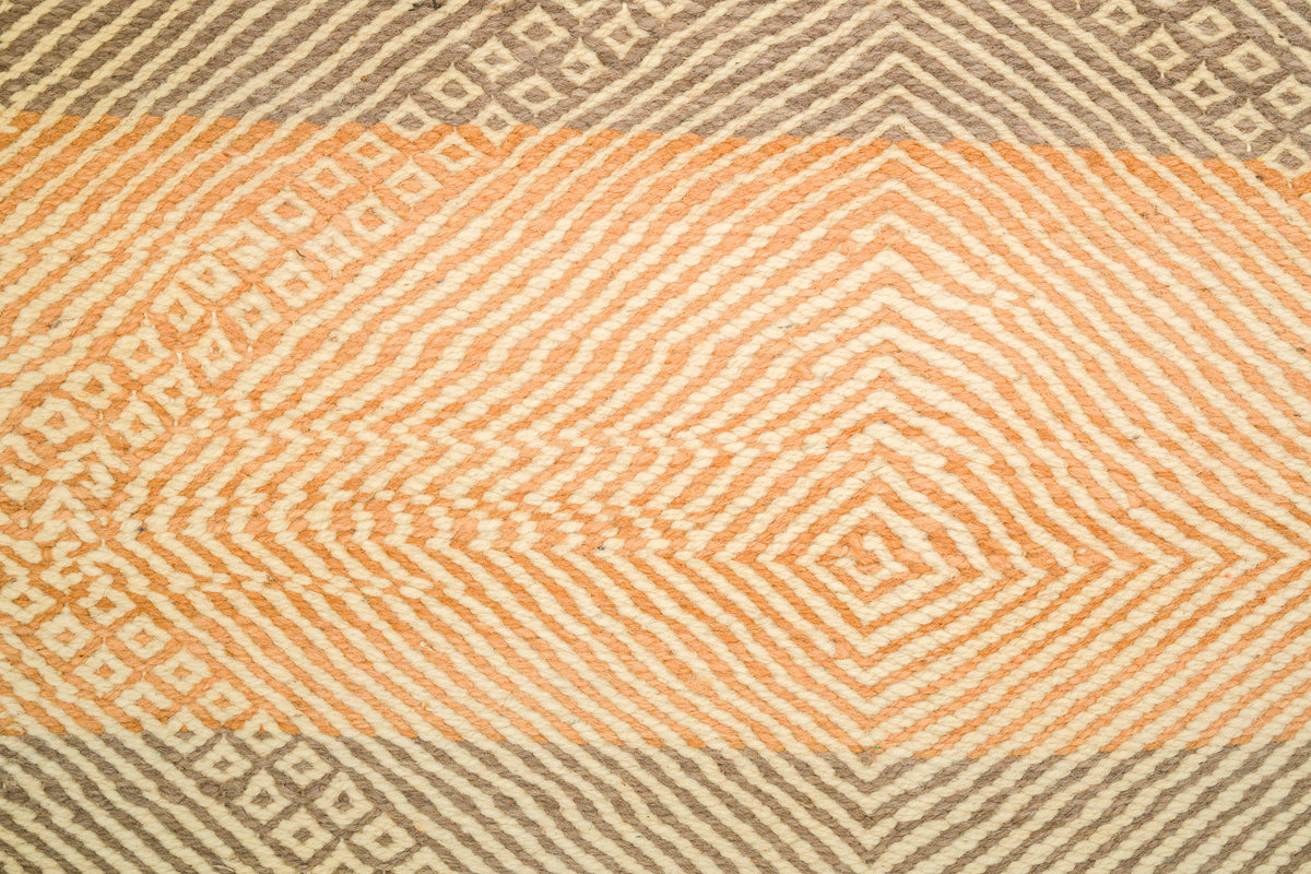 A close-up of a Moroccan Zanafi rug showing a geometric pattern with horizontal bands of peach, cream, and taupe.