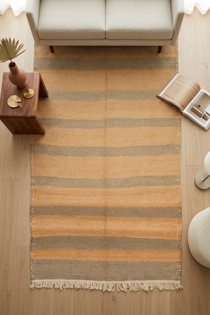 A Zanafi rug with horizontal stripes in beige, tan, and muted brown, laid out on a light wood floor in a styled living room setting.