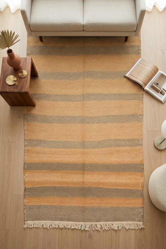 A Zanafi rug with horizontal stripes in beige, tan, and muted brown, laid out on a light wood floor in a styled living room setting.