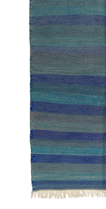 A close-up of aZanafi rug with horizontal stripes in shades of blue, teal, and gray, featuring a textured diamond pattern and off-white fringe at the bottom.