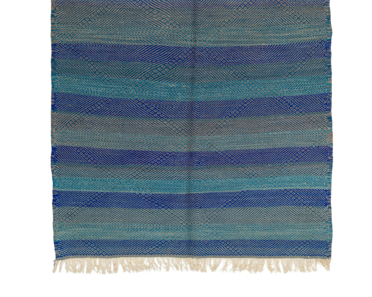 A woven textile with horizontal stripes in shades of blue, teal, and gray, finished with cream-colored fringe at the bottom, shown flat against a white background.