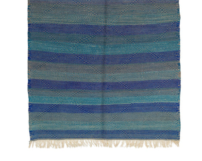 A woven textile with horizontal stripes in shades of blue, teal, and gray, finished with cream-colored fringe at the bottom, shown flat against a white background.