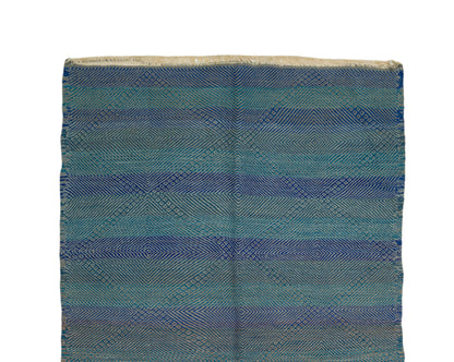 A Zanafi rug featuring a textured geometric diamond pattern in horizontal stripes of blue, teal, and beige on a white background.