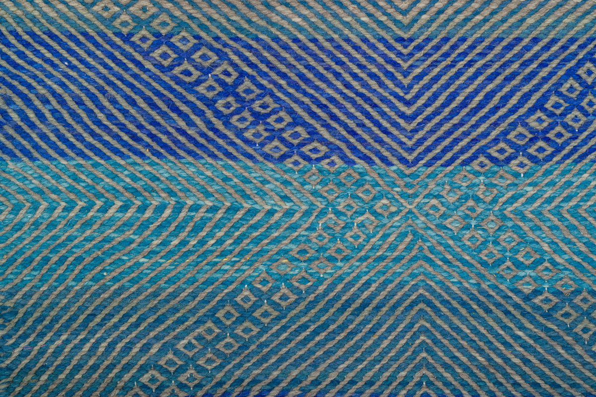 A close-up of Moroccan Zanafi rug with horizontal bands of deep blue, turquoise, and light blue, featuring geometric chevron and diamond motifs in beige.