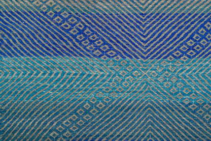 A close-up of Moroccan Zanafi rug with horizontal bands of deep blue, turquoise, and light blue, featuring geometric chevron and diamond motifs in beige.