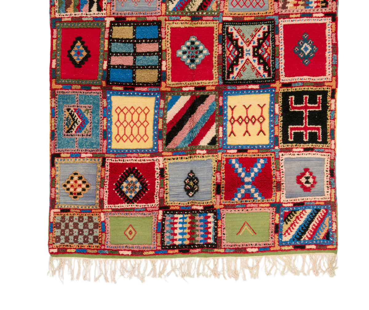 A handwoven Moroccan rug with a patchwork design of colorful geometric panels and white fringe tassels at the bottom, shown flat against a white background.