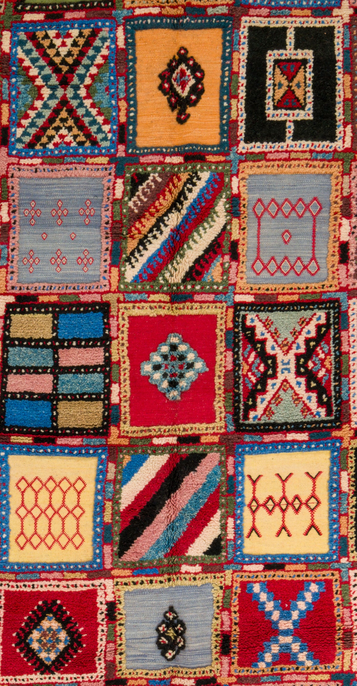 A close-up of a colorful patchwork rug featuring multiple square panels with geometric and tribal-inspired patterns in red, blue, yellow, black, beige, and pink.