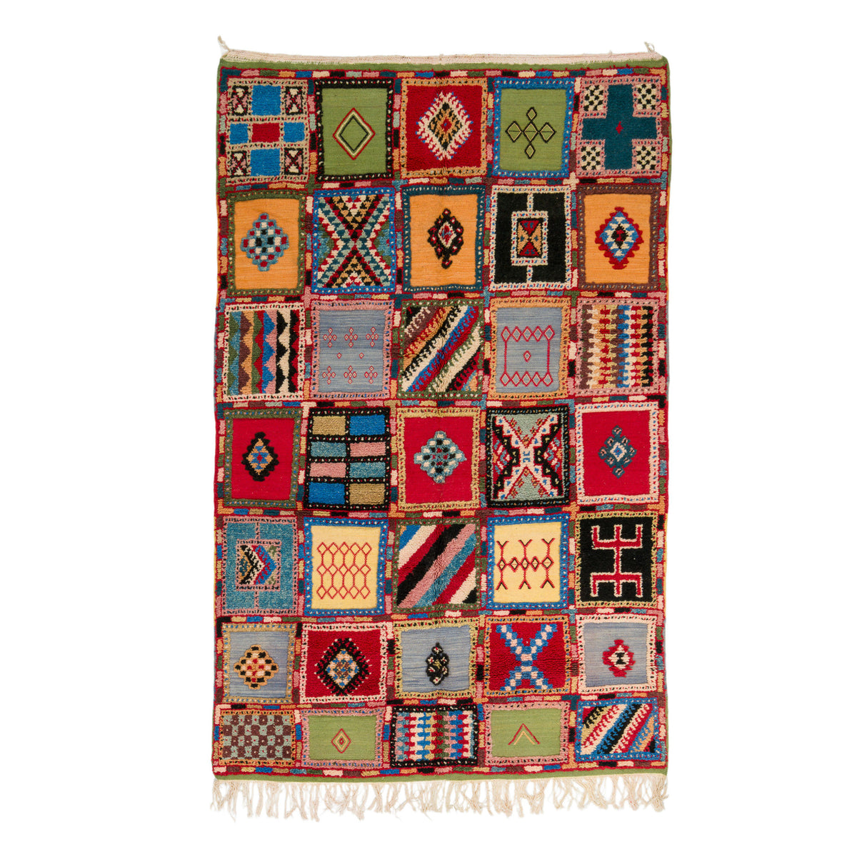 A multicolor patchwork-style woven rug with geometric diamond and striped motifs in red, blue, green, black, beige, and orange, finished with white fringe on the top and bottom, shown against a plain white background.