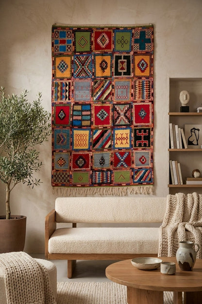 A colorful patchwork-style woven wall hanging with geometric patterns and fringe, displayed above a cream upholstered sofa in a warm, styled living room.