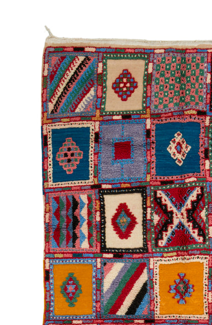 A close-up of a colorful Moroccan-style woven rug with a patchwork design of geometric square panels in blue, red, yellow, green, and cream.