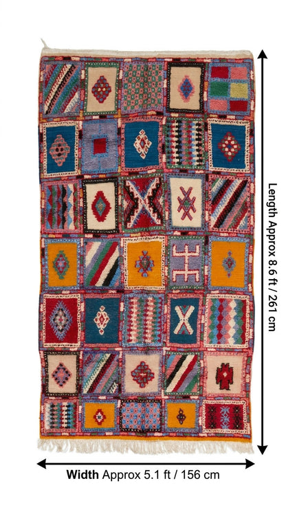 A rectangular patchwork-style woven rug with many colorful geometric and diamond motifs, shown flat against a white background with measurement arrows.