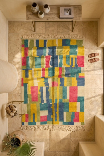 A colorful geometric area rug with fringe, displayed in a styled home entryway with a stone tile floor, a wooden bench, and decorative accessories.