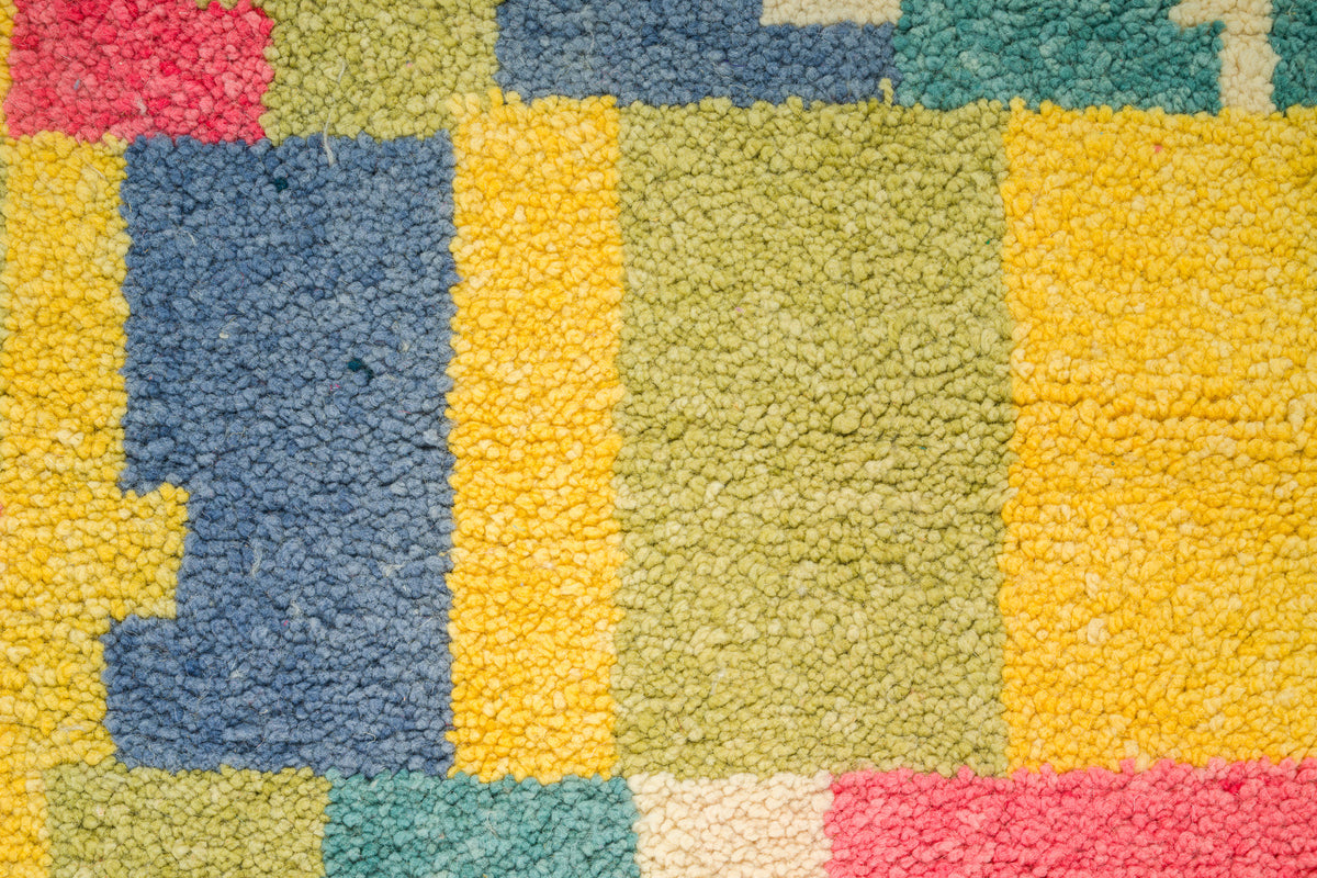 Close-up of a colorful textured rug with a geometric patchwork pattern in yellow, blue, green, pink, and cream.