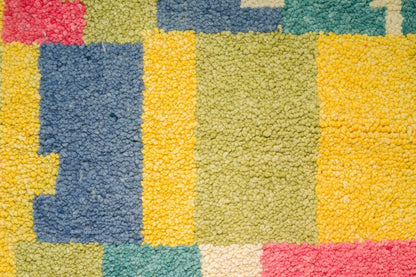 Close-up of a colorful textured rug with a geometric patchwork pattern in yellow, blue, green, pink, and cream.