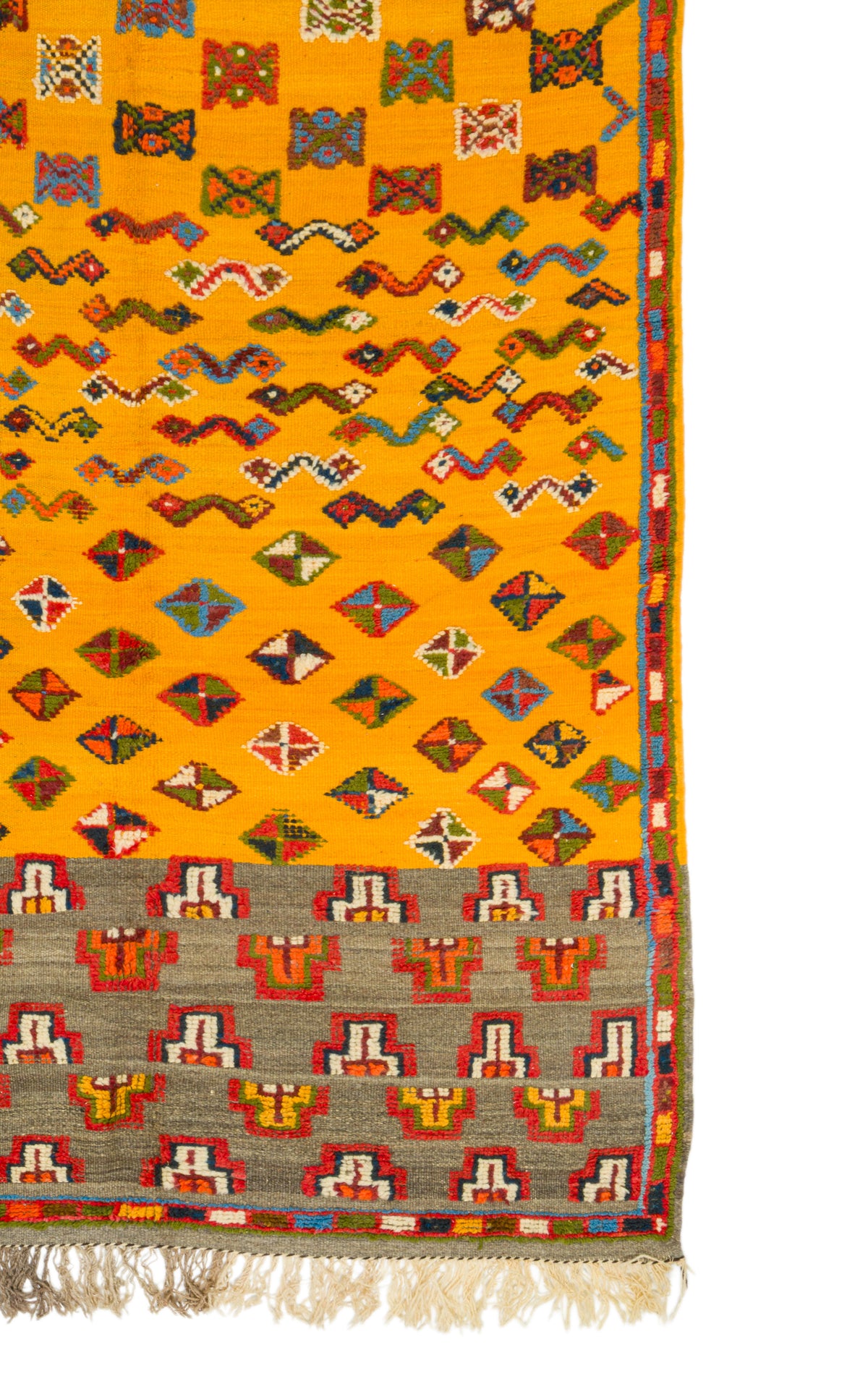 A close-up of a woven rug with a bright yellow field, repeating multicolor geometric motifs, a gray patterned border, and cream fringe at the bottom.