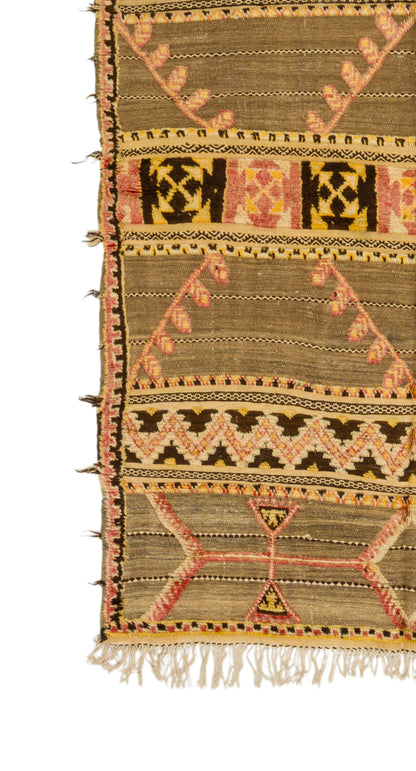 A close-up of a patterned woven vintage moroccan kilim rug showing a detailed section with geometric and tribal-inspired motifs in brown, beige, pink, and black, finished with a fringed edge.