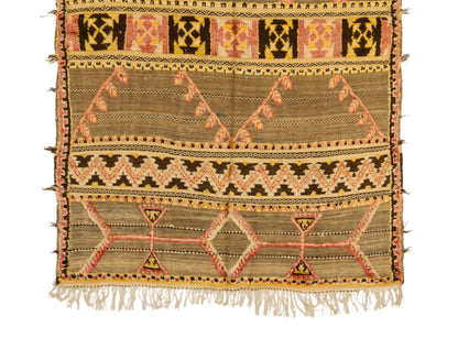A vintage moroccan kilim rug featuring geometric and tribal-inspired patterns in beige, brown, orange, and black on a white background.