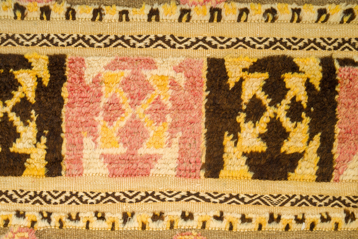 A close-up of a vintage moroccan kilim rug featuring geometric patterns in dark brown, pink, yellow, and cream.