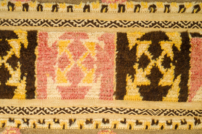 A close-up of a vintage moroccan kilim rug featuring geometric patterns in dark brown, pink, yellow, and cream.