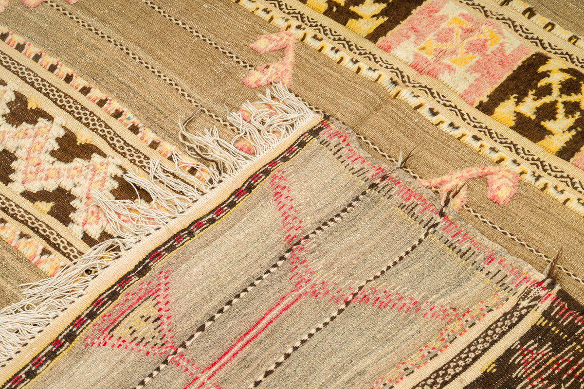 A close-up of a vintage moroccan kilim rug with a geometric tribal pattern in beige, brown, pink, and cream, showing fringed edges and detailed textile construction.