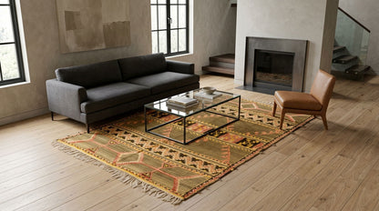 A vintage moroccan kilim rug styled in a  living room scene featuring a dark gray fabric sofa, a brown leather accent chair. Geometric tribal pattern in beige, orange, and brown tones. A modern glass-top coffee table sits on the rug, all set on light wood floors in front of a fireplace.