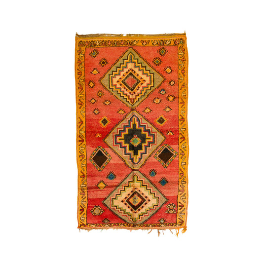 A vintage Taznakht wool rug from Morocco with a terracotta red center, featuring three large geometric diamond medallions and a wide golden-yellow border, isolated on a white background.