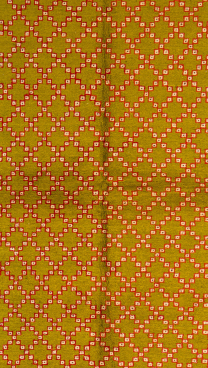 A close-up of a vintage Moroccan rug featuring a repeating geometric diamond lattice design in olive green, orange, and white.