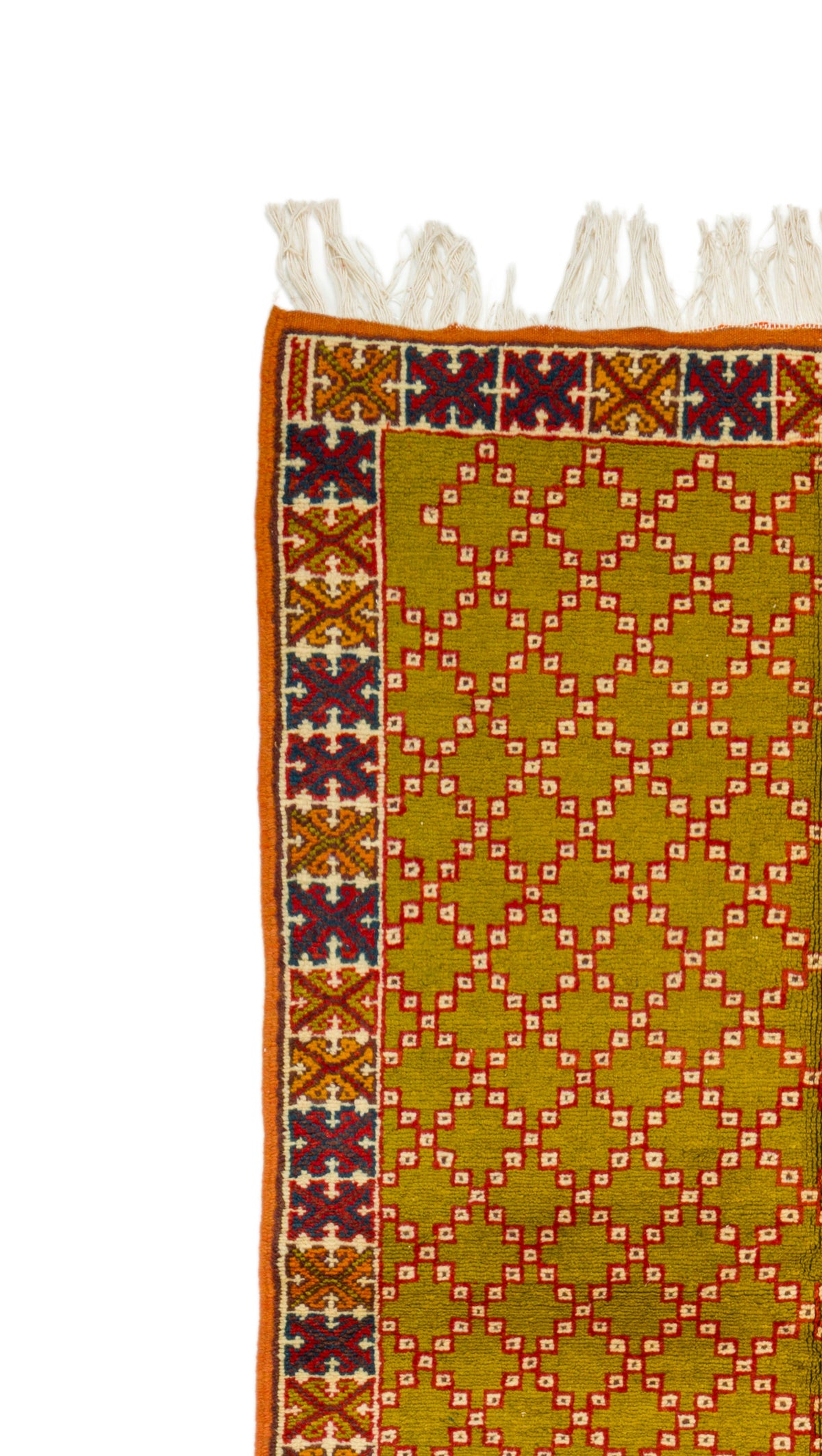 A close-up of a patterned rug showing a mustard yellow field with a repeating diamond lattice in red and white, bordered by a multicolor geometric pattern and white fringe tassels at the top.