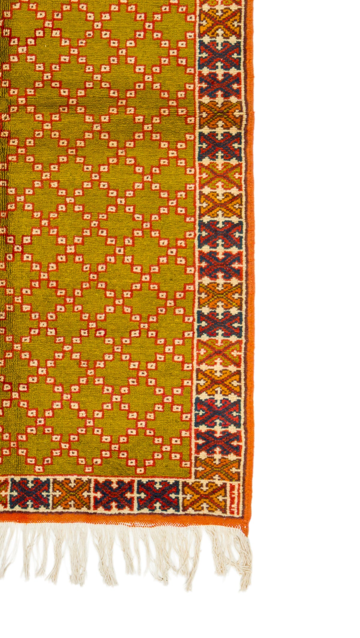 A close-up of a patterned rug featuring a mustard yellow-green field with a repeating diamond lattice in orange and white, finished with a decorative border in orange, brown, and cream, and white fringe tassels at the bottom.