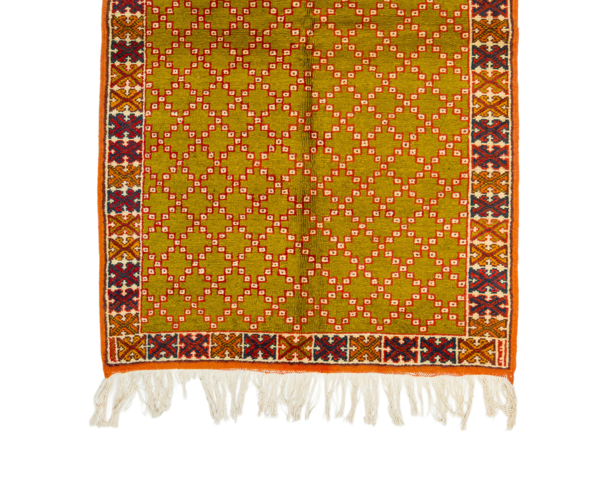 A Moroccan vintage rug with fringe, featuring a mustard yellow center with a repeating diamond lattice pattern in orange, white, and red, bordered by a multicolor geometric pattern and white tassels.
