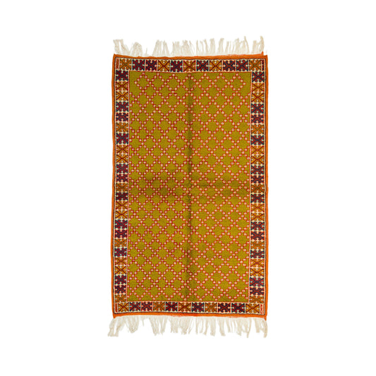 A rectangular woven textile with cream fringe on both ends, featuring a mustard yellow field with a repeating small geometric pattern and a decorative border in orange, burgundy, and cream.