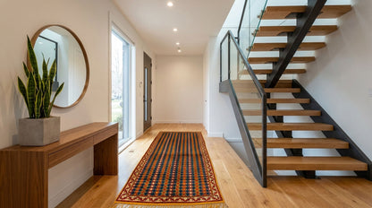A modern staircase with light wood steps and black metal railings in a bright hallway with hardwood floors and a patterned runner Taznakht rug.