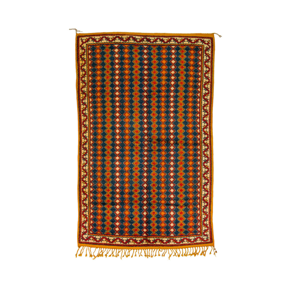 This one-of-a-kind 1970s vintage Moroccan wool rug was hand-knotted by a Berber woman artisan in the High Atlas Mountains of Morocco using traditional Taznakht rug-making techniques.
A rectangular woven rug with a geometric pattern in navy blue, rust orange, and cream, featuring a decorative border and fringe on a white background.