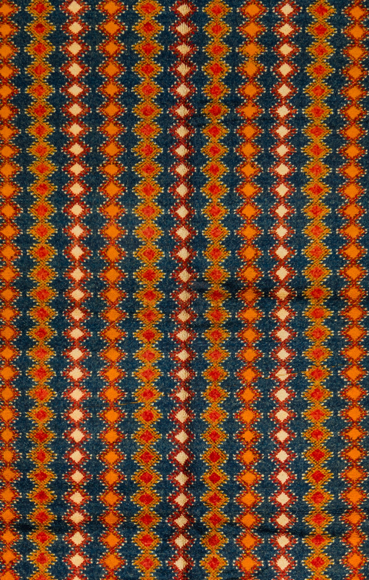 A close-up of a patterned Taznakht vintage rug featuring vertical columns of repeating diamond motifs in orange, red, cream, and dark navy blue.