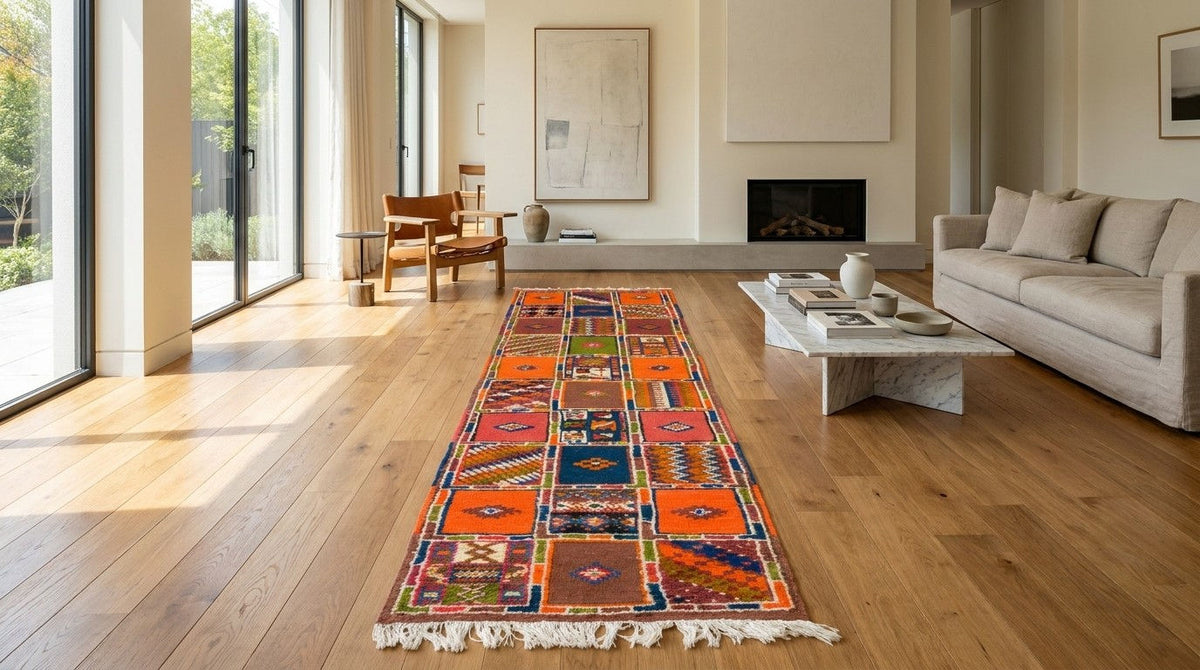 A long, colorful patchwork runner rug with white fringe is displayed on a light wood floor in a bright, modern living room with a sofa, coffee table, and fireplace.