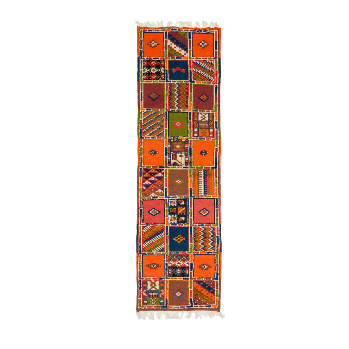 A long rectangular kilim runner rug with a vibrant patchwork design of orange, red, blue, green, and brown geometric squares, finished with white fringe on the top and bottom.