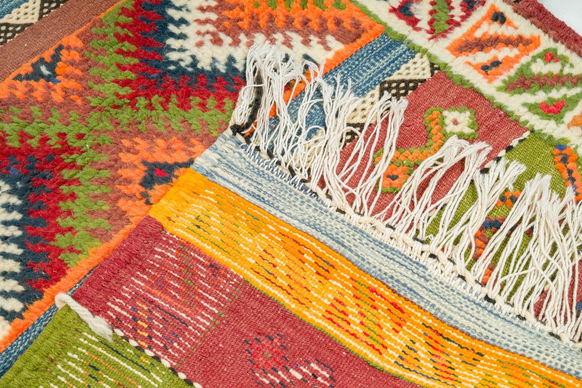 Close-up of a colorful woven rug with geometric patterns and white fringe tassels.